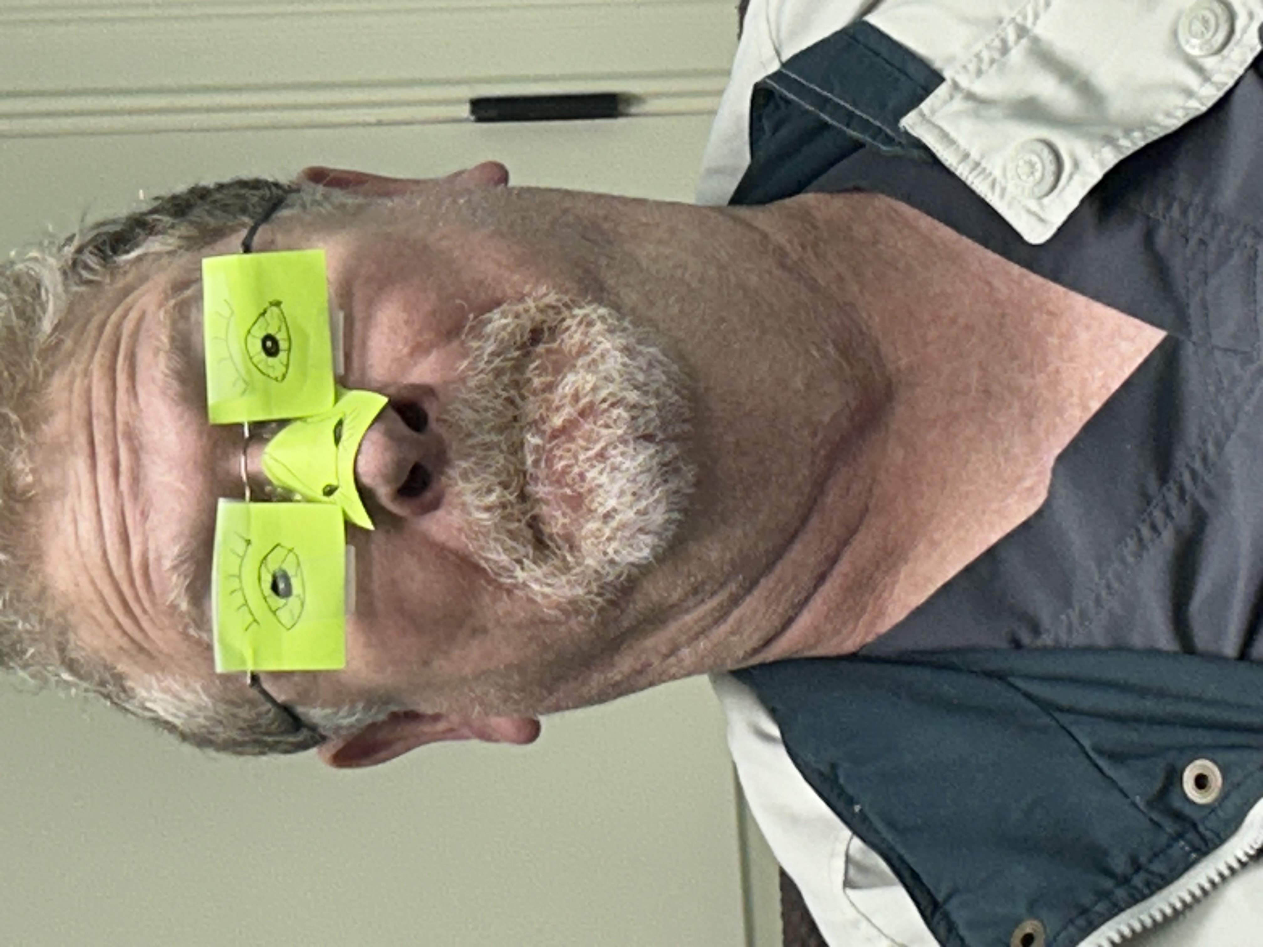 Old man with sticky sotes with eyes scribbled on them covering his glasses.